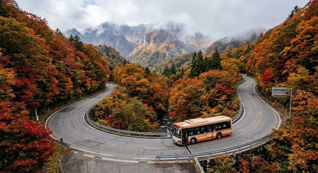 An aerial view of a mountain road winding through vibrant red and gold autumn forests in Nagano, showing a local transit bus navigating towards misty mountain peaks.