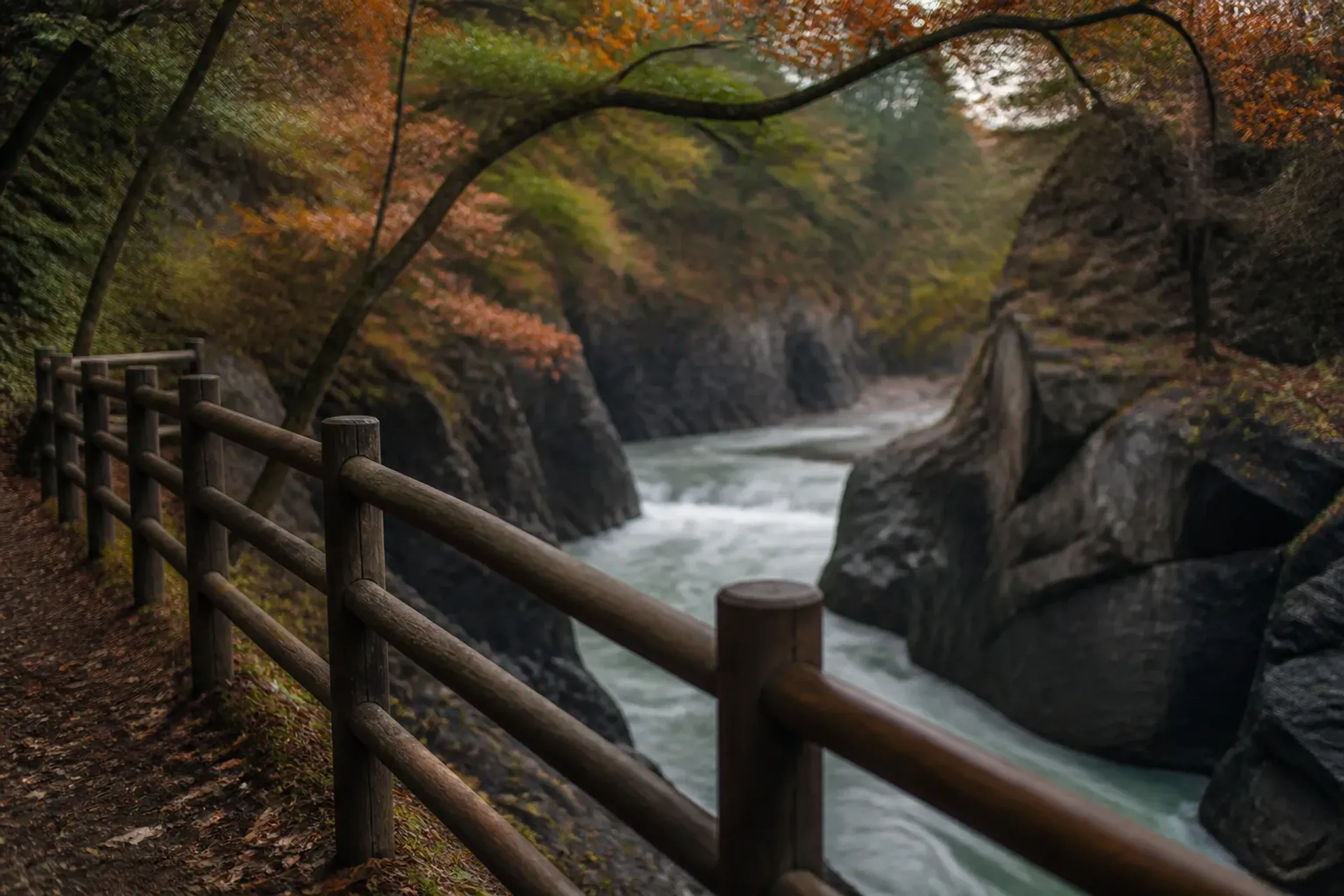A short, level riverside path viewpoint at Genbikei Gorge in Iwate: the pedestrian edge/railing overlooking the rushing water and ink-dark rock formations under late-season foliage, composed without p