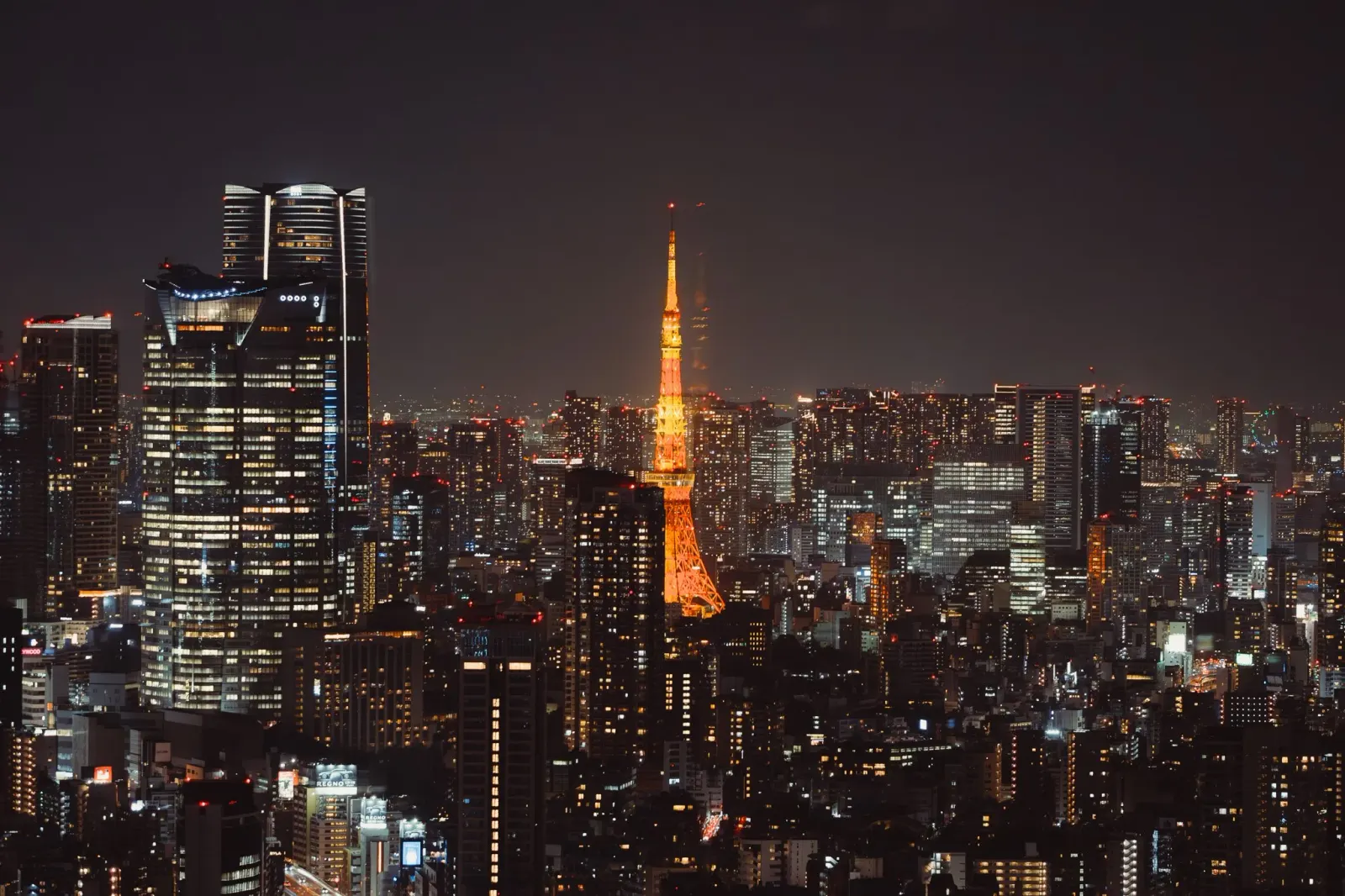 Tokyo Tower glowing amber above the night skyline, seen from altitude