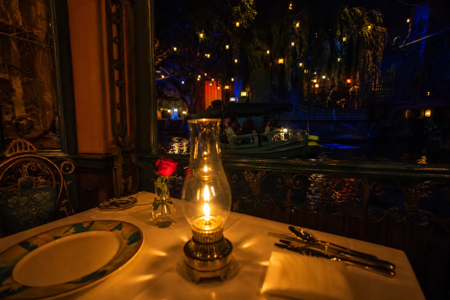 Lakeside outdoor restaurant at night with warm lanterns and candlelit tables along the water's edge.