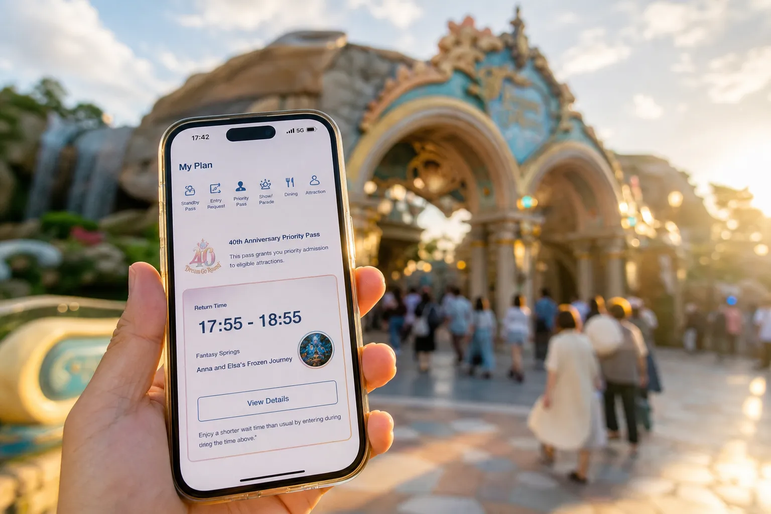 The Tokyo Disney Resort App open to the 'My Plan' screen displaying the 40th Anniversary Priority Pass return-time interface, held in hand against a blurred backdrop of Tokyo DisneySea's Fantasy Sprin