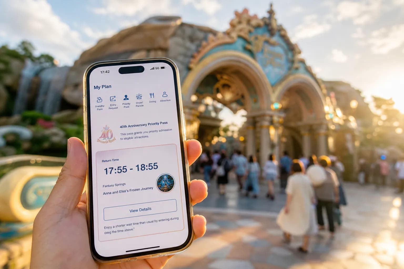 The Tokyo Disney Resort App open to the 'My Plan' screen displaying the 40th Anniversary Priority Pass return-time interface, held in hand against a blurred backdrop of Tokyo DisneySea's Fantasy Sprin