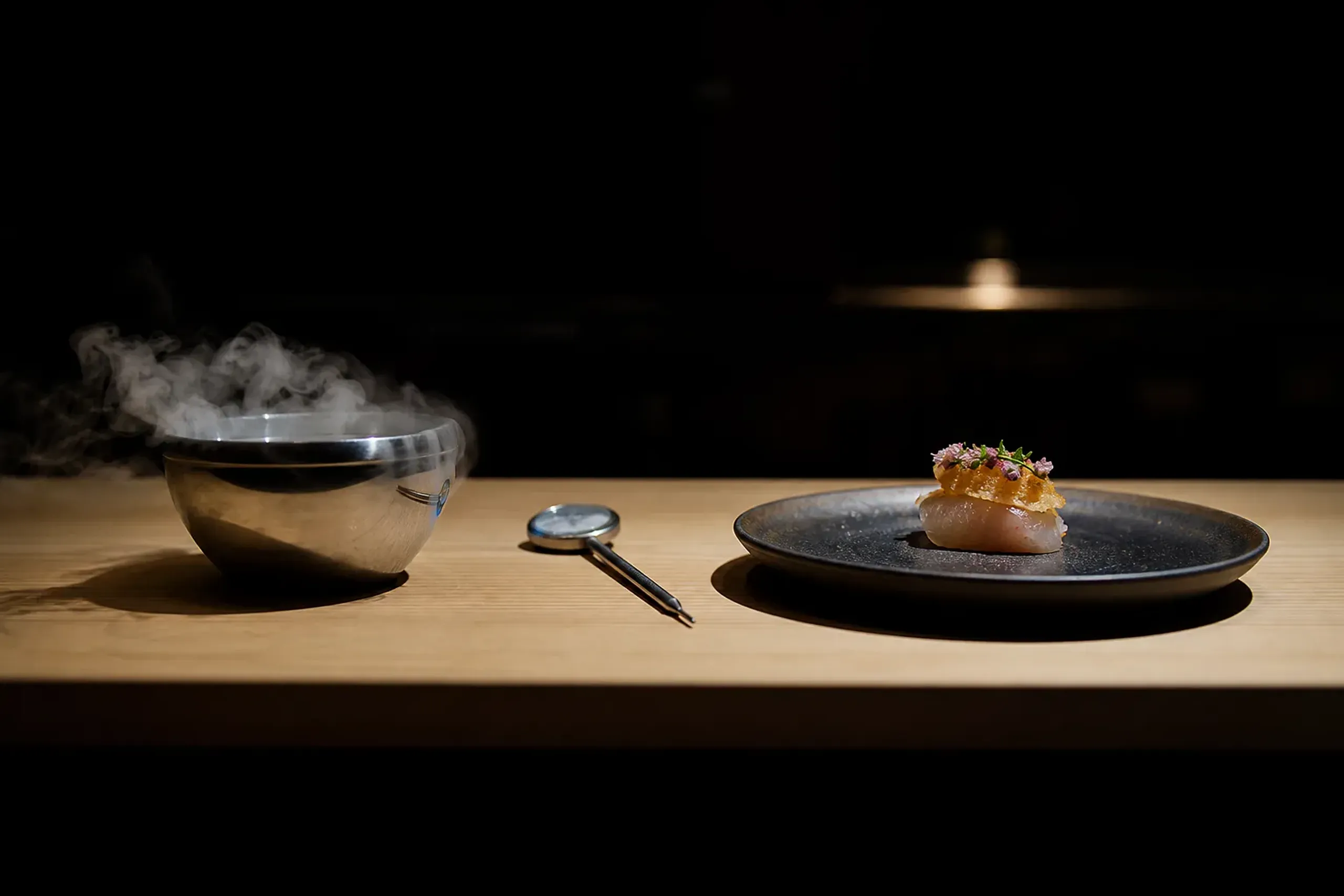 Modern culinary tools and a plated bite on a chef’s counter in Tokyo, suggesting liquid nitrogen technique with Japanese ingredients