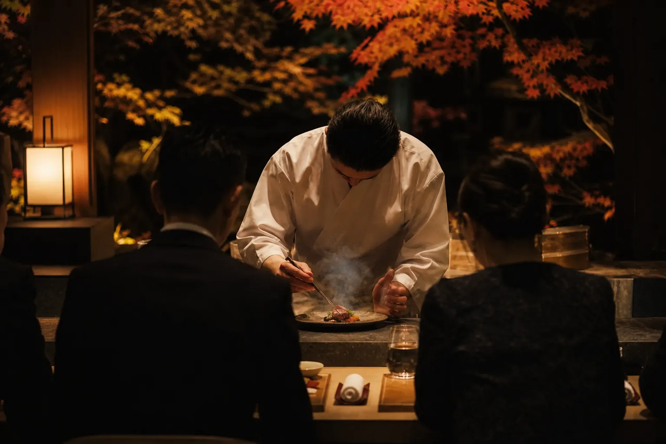 Guests seated at an intimate counter facing chefs plating small courses inside a luxury hotel in Tokyo