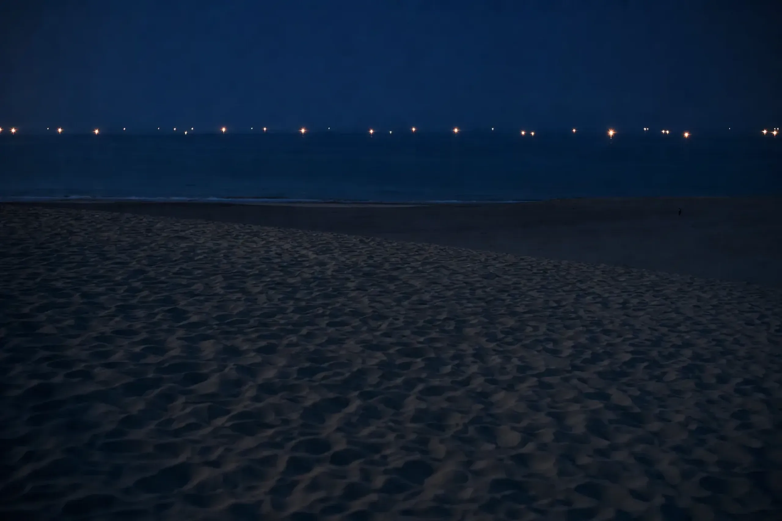scattered isaribi fishing boat lamps glowing on the dark Sea of Japan viewed from the cooling night dunes