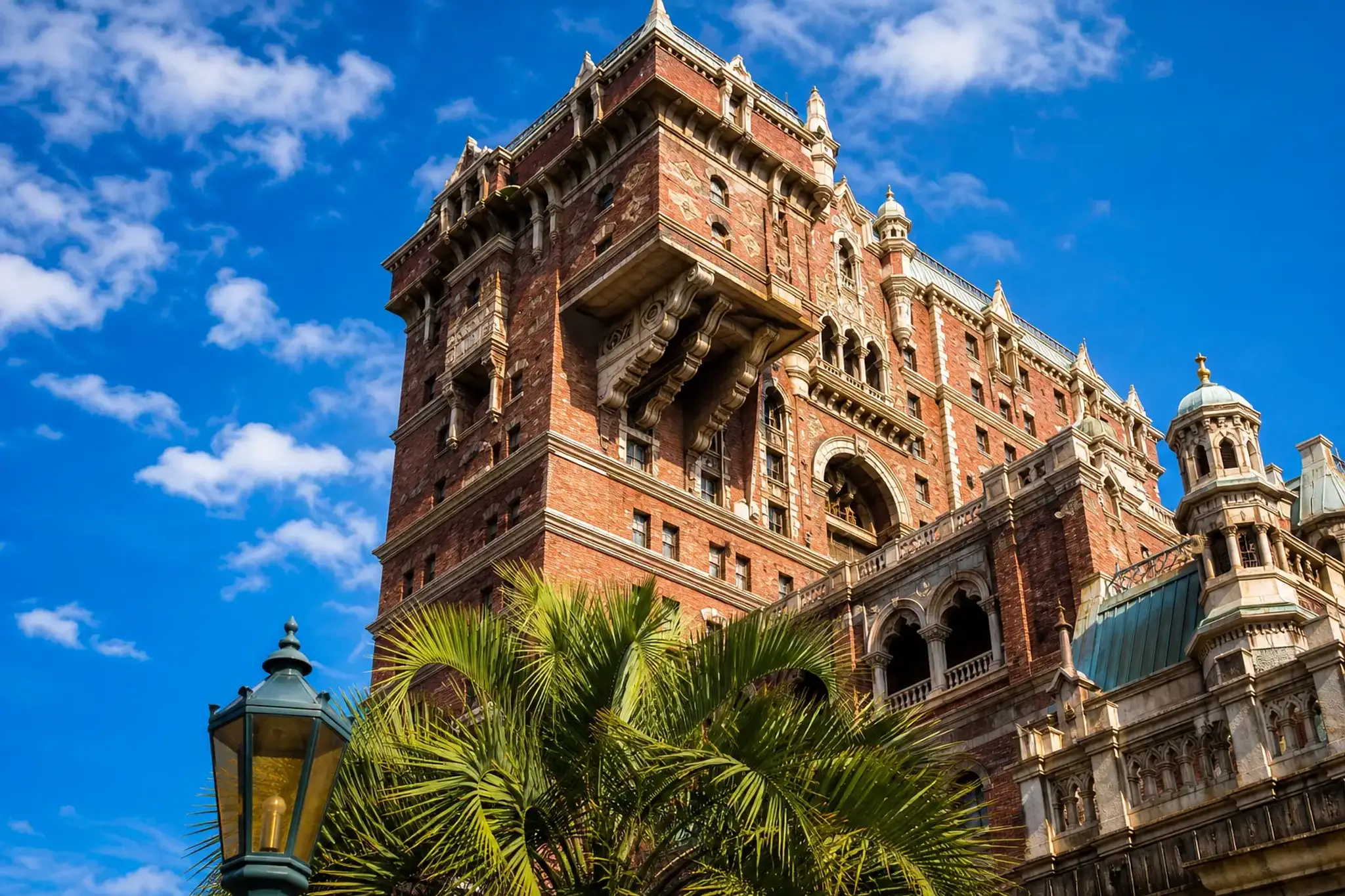 The towering brick exterior of the Hotel Hightower ride building housing the Tower of Terror attraction at Tokyo DisneySea, with its ornate gothic facade and weathered stonework rising against a brigh