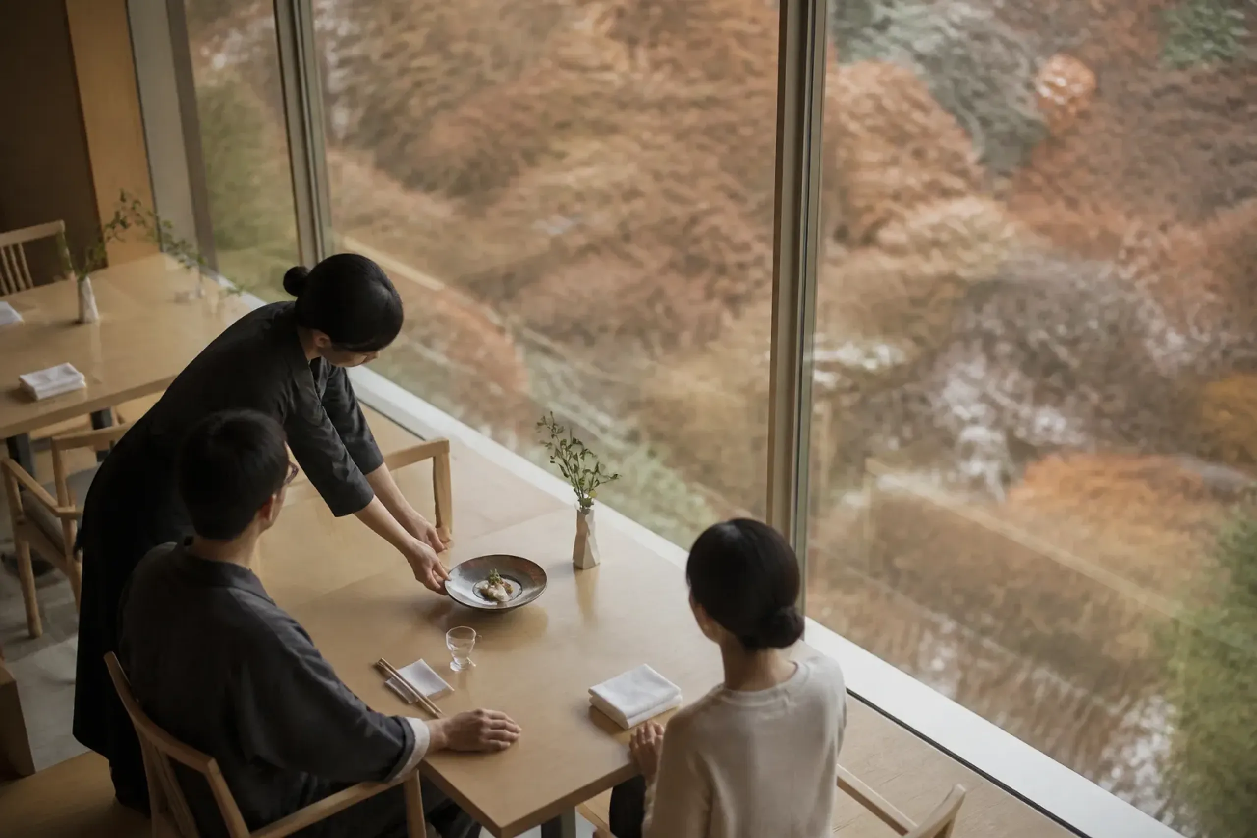 A modern ryokan restaurant with individual tables and windows overlooking an autumn landscape
