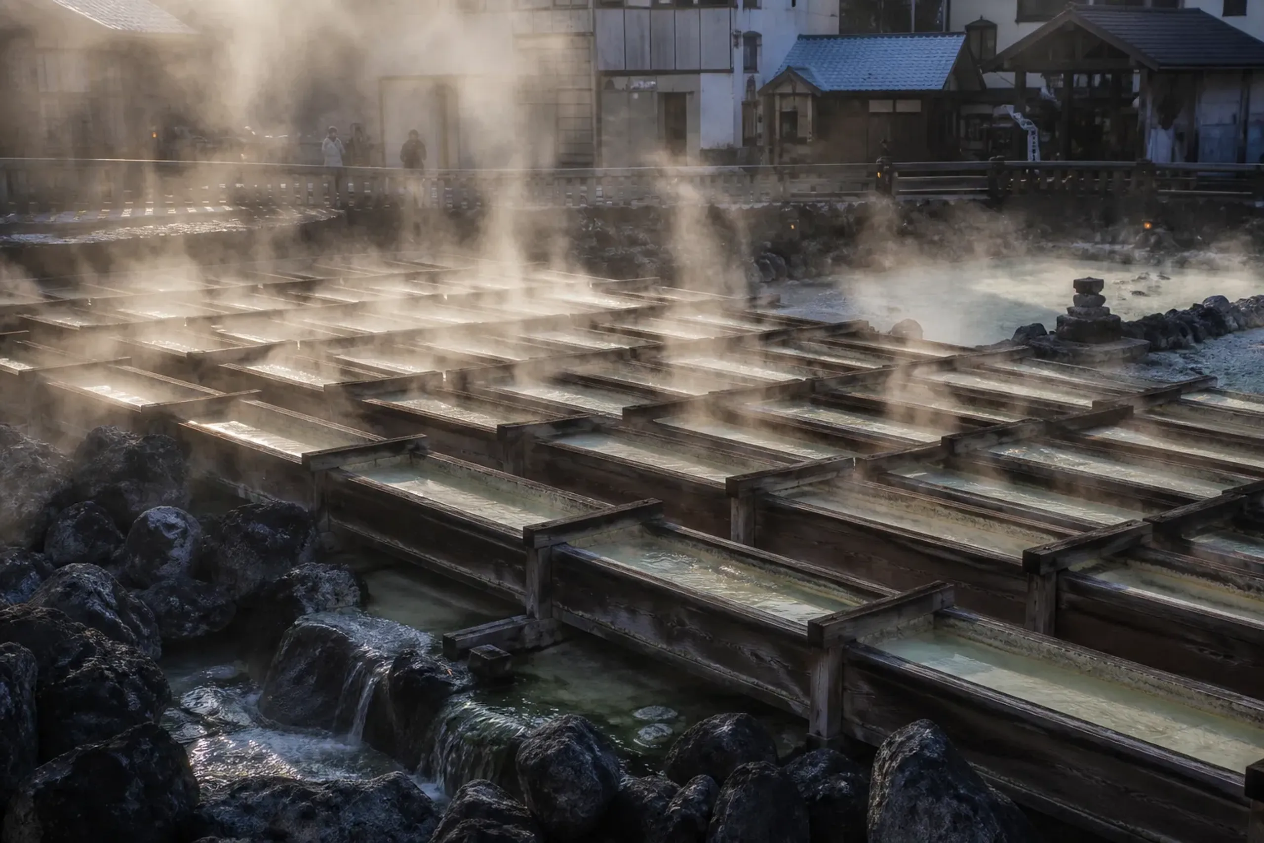 The Yubatake hot water fields in Kusatsu Onsen with steam rising from wooden channels in the morning