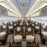 Interior of a modern airplane cabin with many brown leather seats and overhead bins.