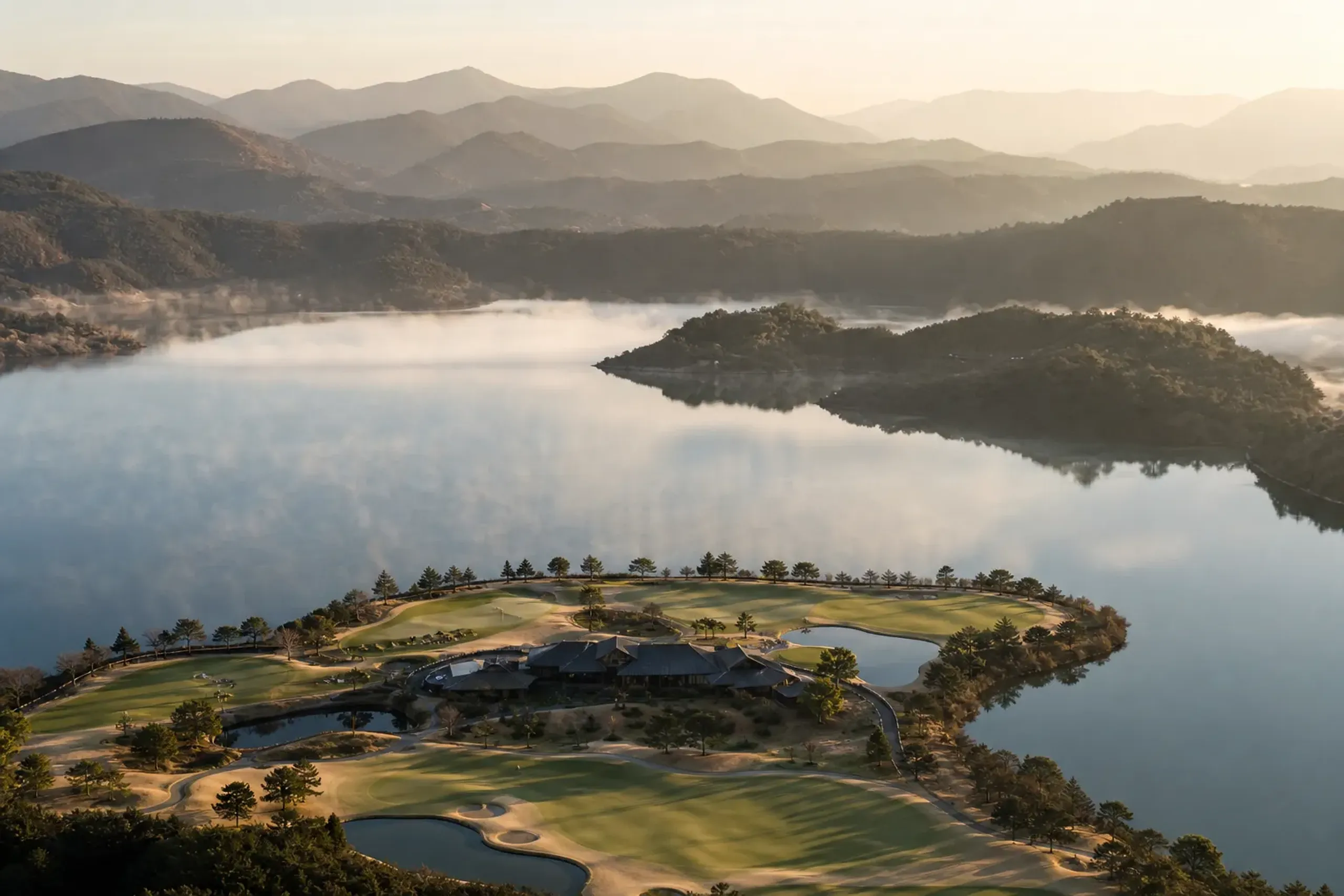 Aerial shot of a luxury golf resort situated next to a large lagoon and rolling mountains.