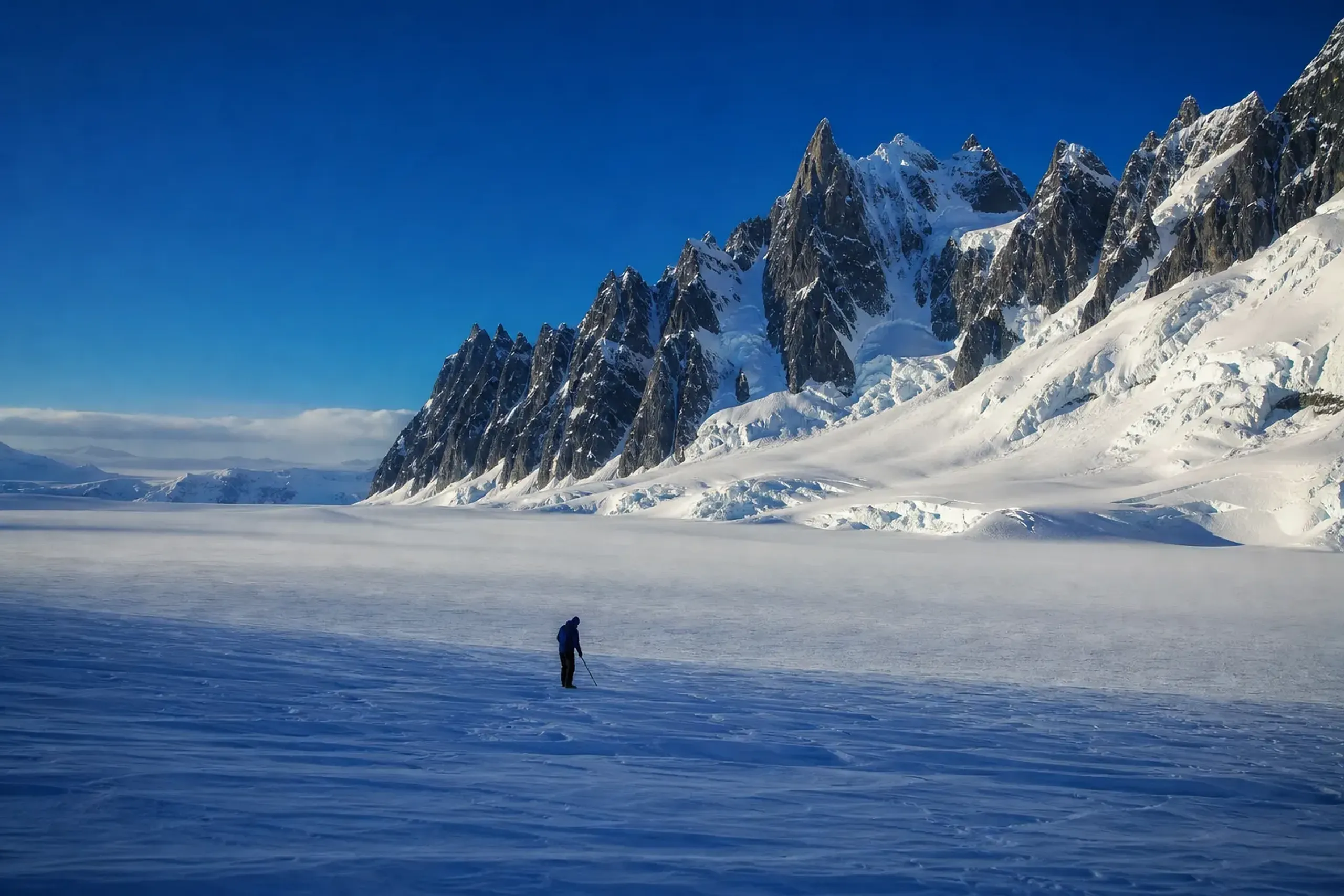 Majestic jagged rocky mountains covered in thick snow and ice under a blue Antarctic sky.