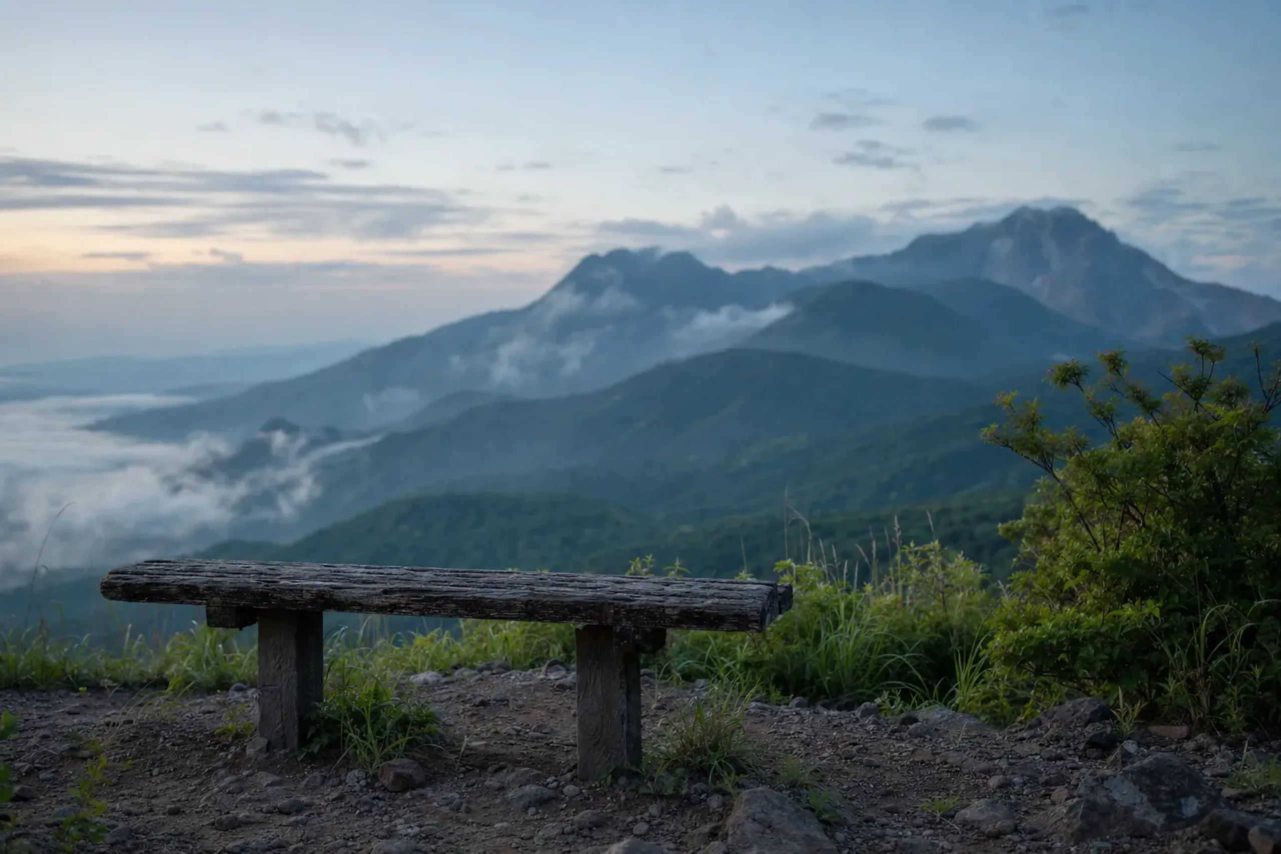A solitary wooden bench set beside a cool highland trail overlooking the green ridgeline of Unzen