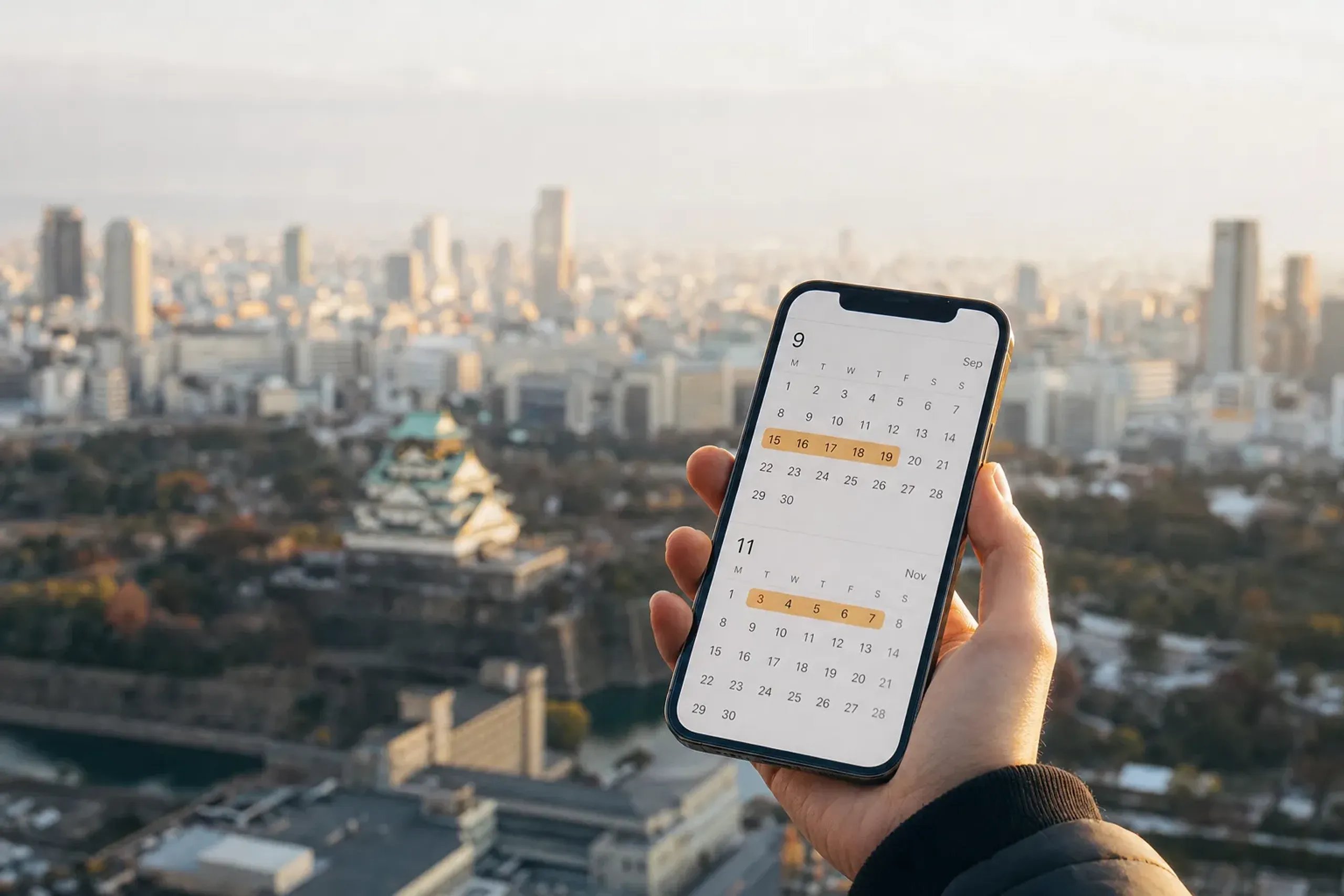 Hand holding a phone displaying a calendar with September to November dates highlighted for trip planning