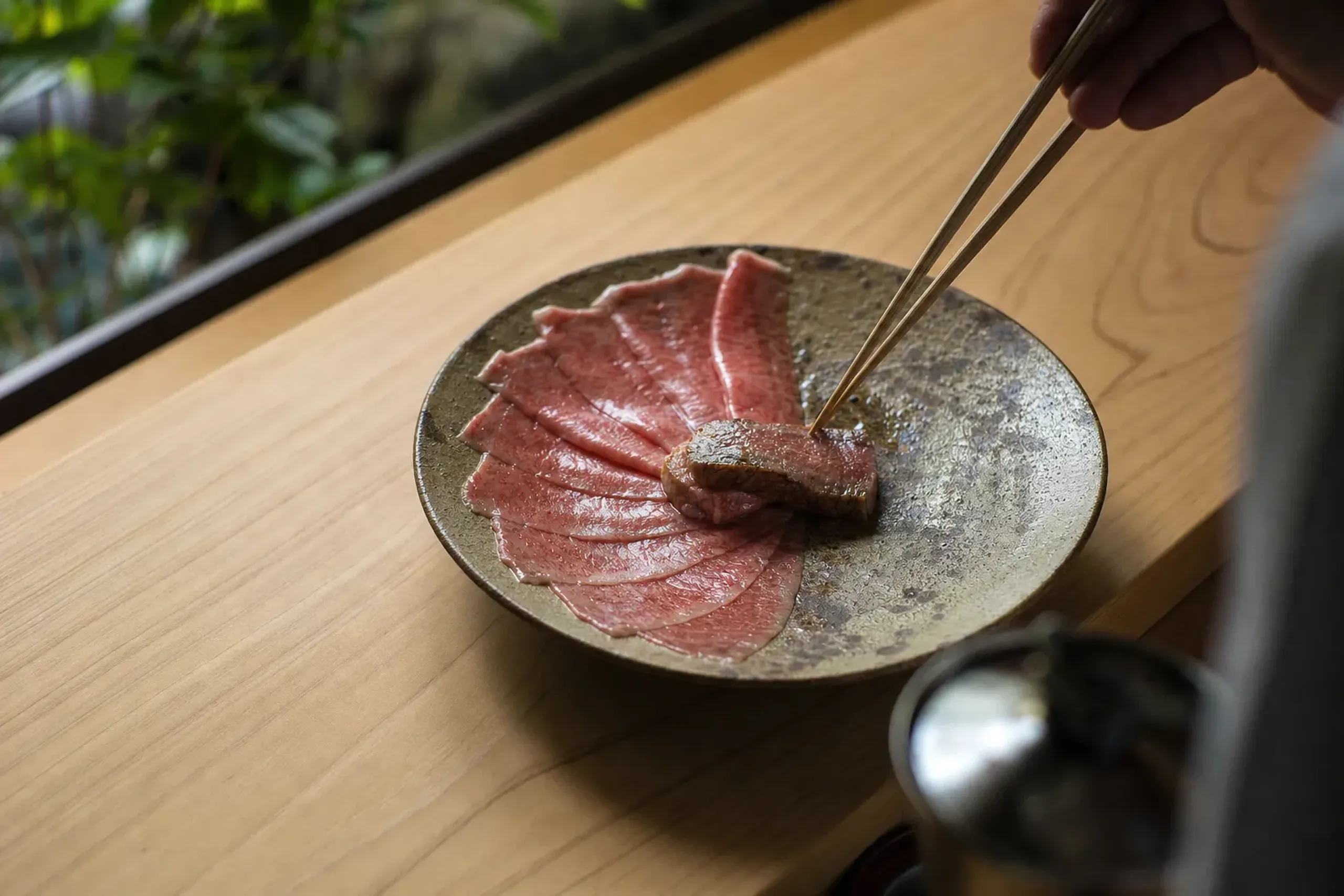 a private chef's-table counter with thin slices of raw wagyu sashimi and a lightly seared marbled central cut arranged on a ceramic plate