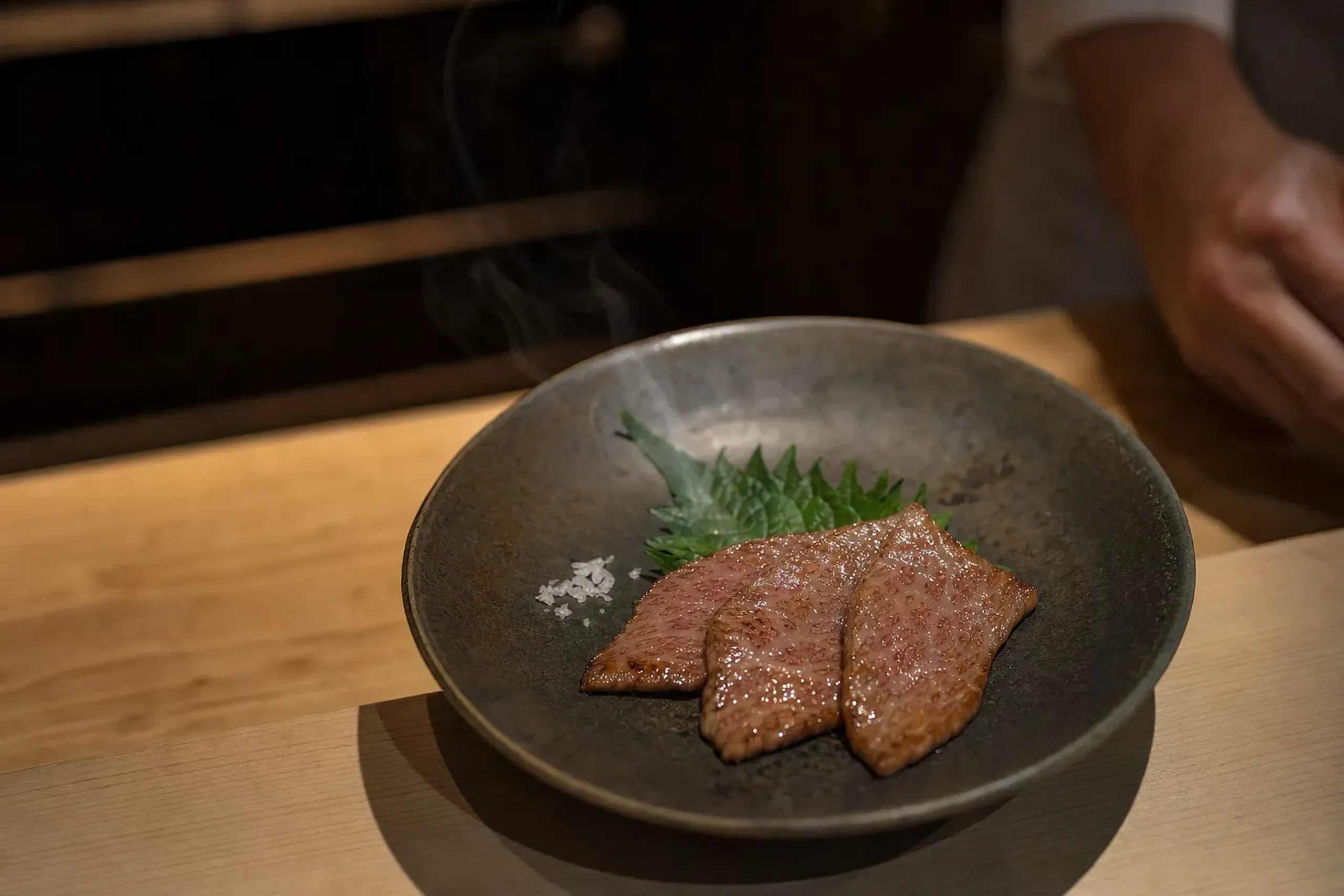 an intimate chef's counter setting with a single portion of grilled wagyu plated in restrained wabi-sabi style