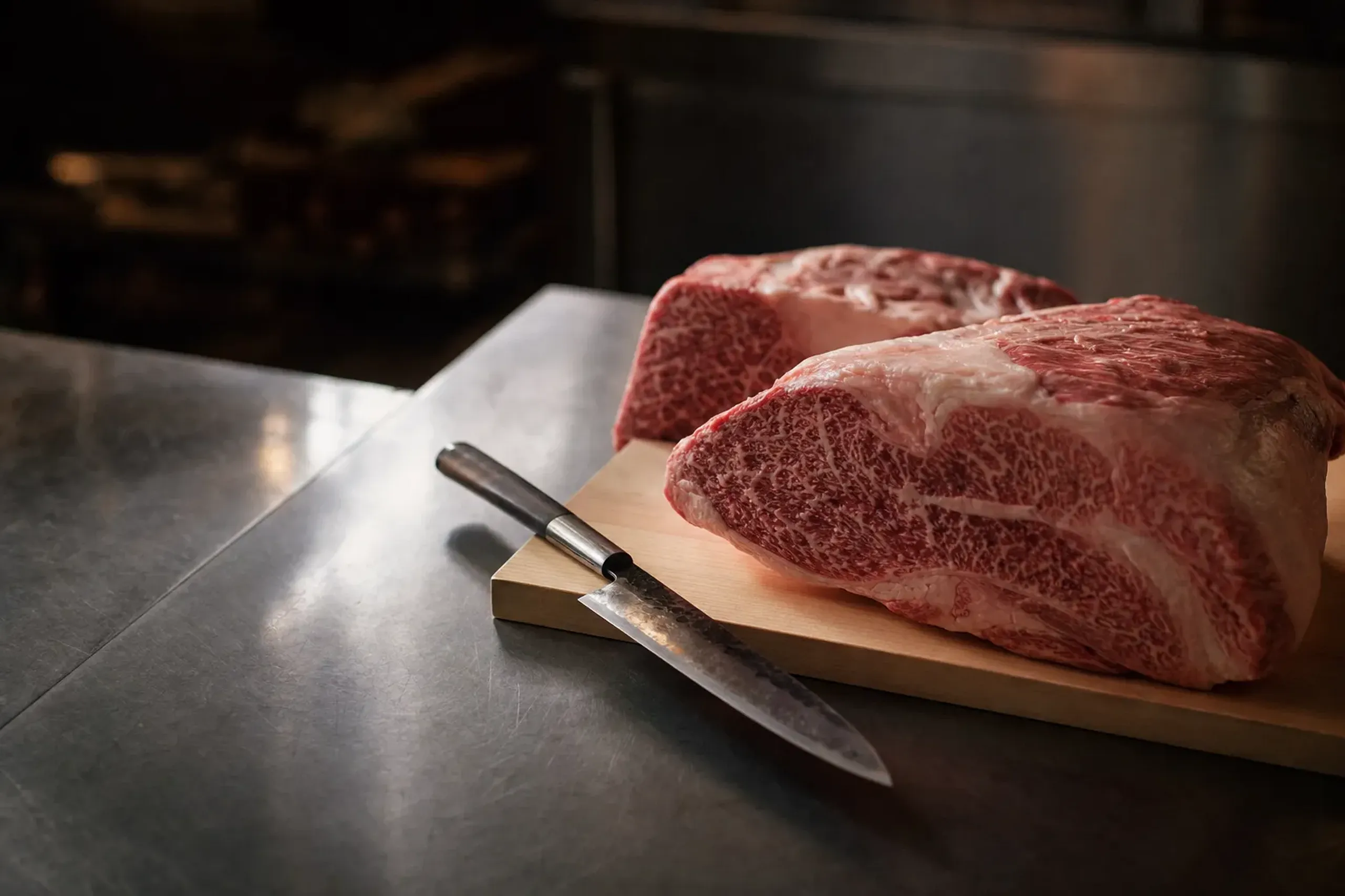 a butcher's block with whole primal cuts of wagyu and a traditional Japanese knife on a clean steel table