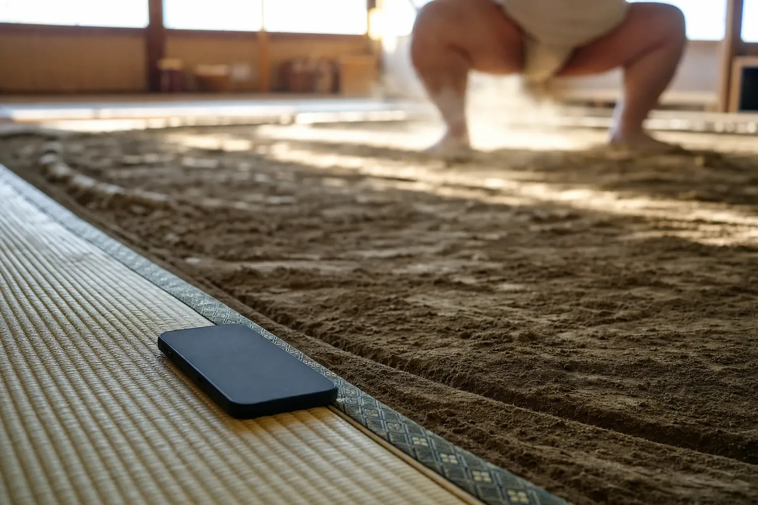 a silenced smartphone lying face-down and switched off on the tatami edge of a sumo stable training floor