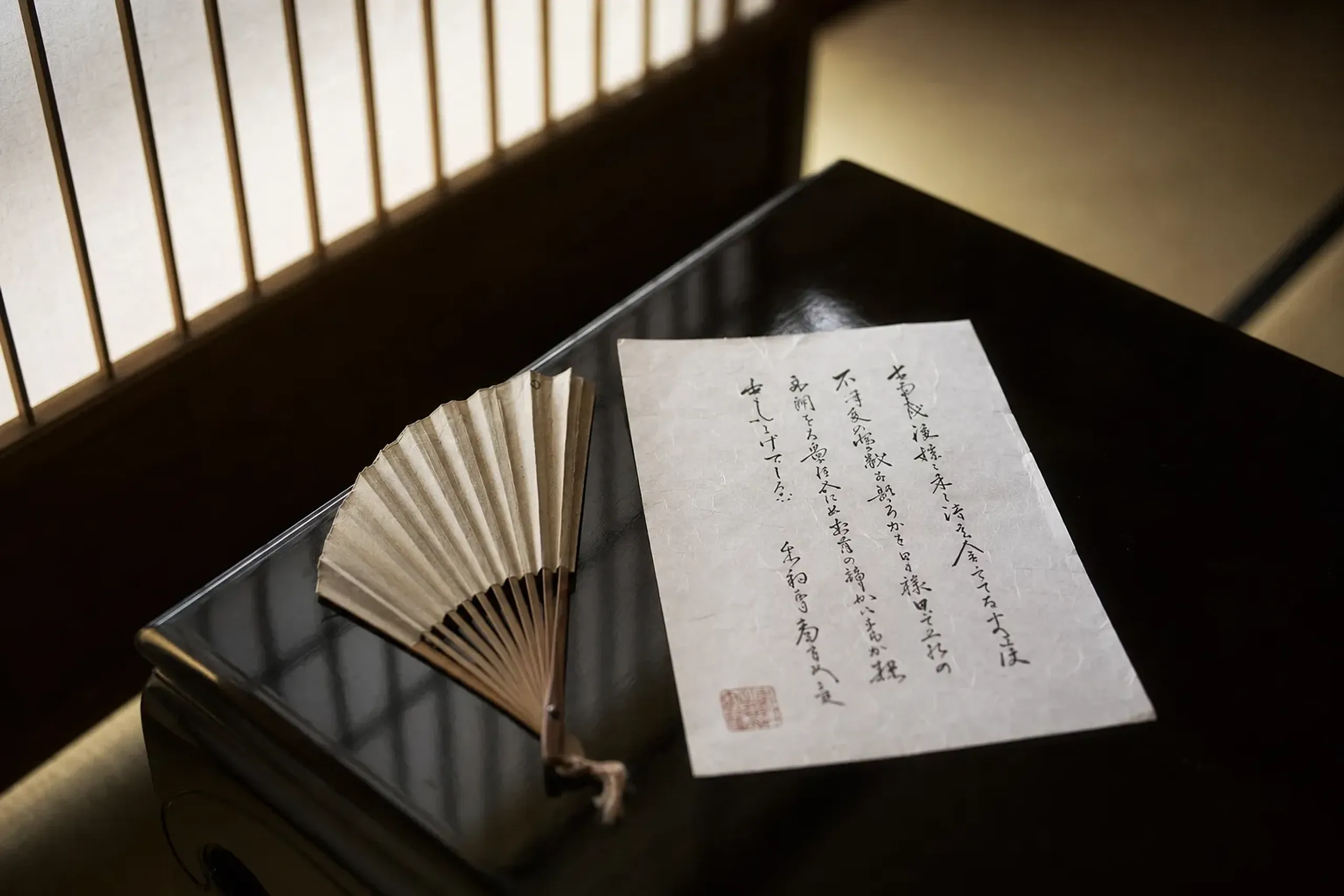 a formal handwritten letter of introduction with an inkan seal resting beside a folded fan on a low lacquered table