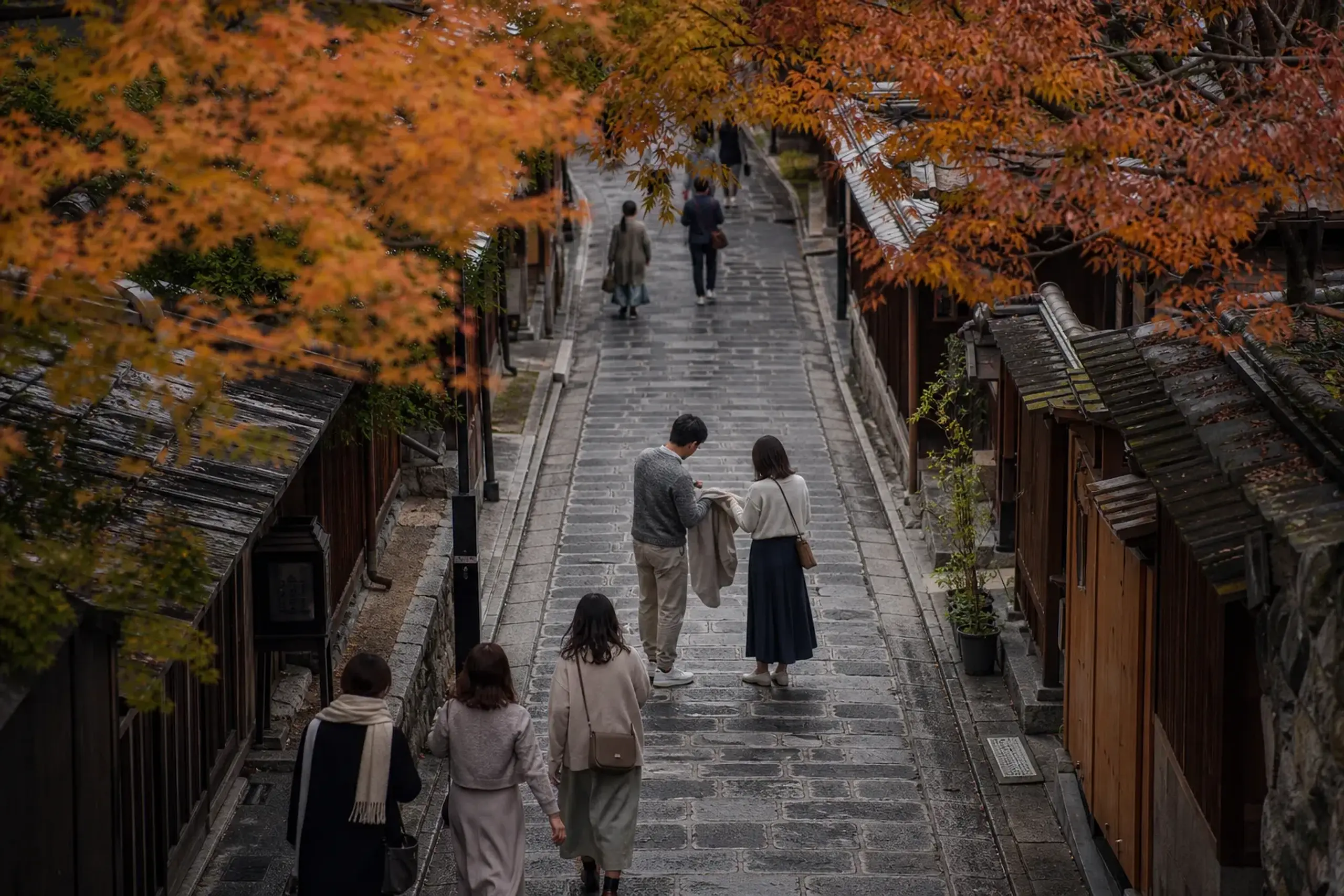 Travelers in light layers walking a stone-paved Kyoto lane during autumn shoulder season
