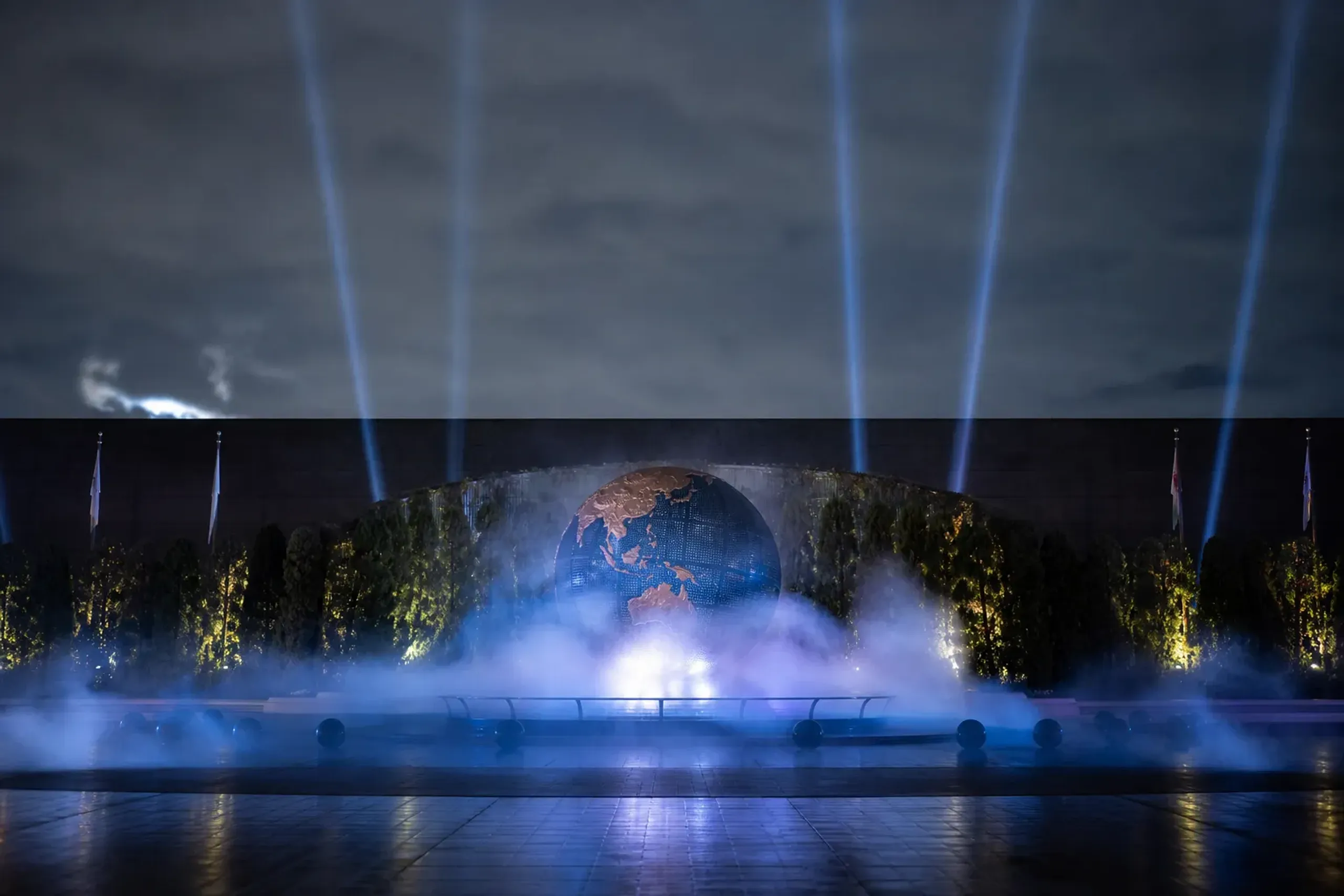 Fog machines exhaling low mist across the front gates of Universal Studios Japan at dusk, the sky the colour of cooled iron