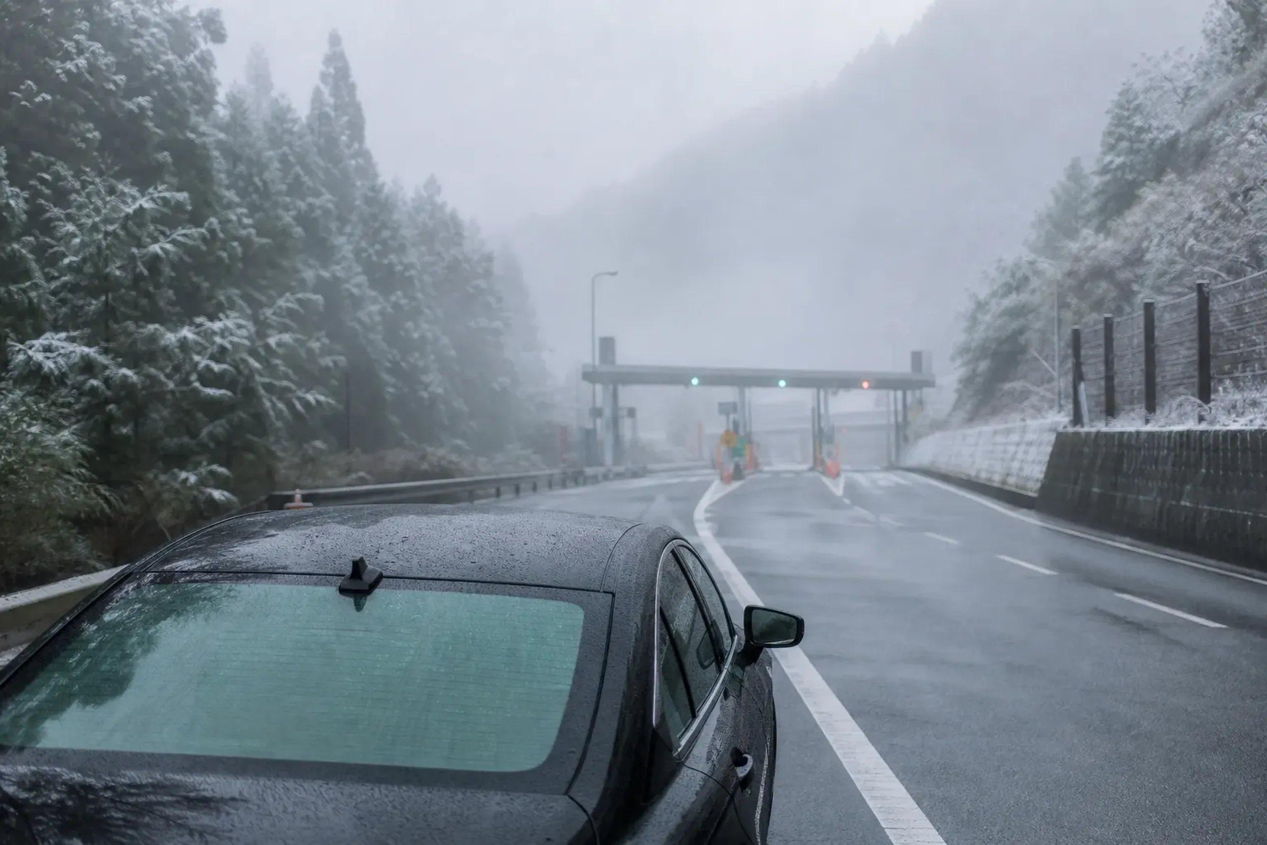 A narrow rural mountain pass road in Japan winding through misty forested slopes with an ETC expressway toll gate ahead