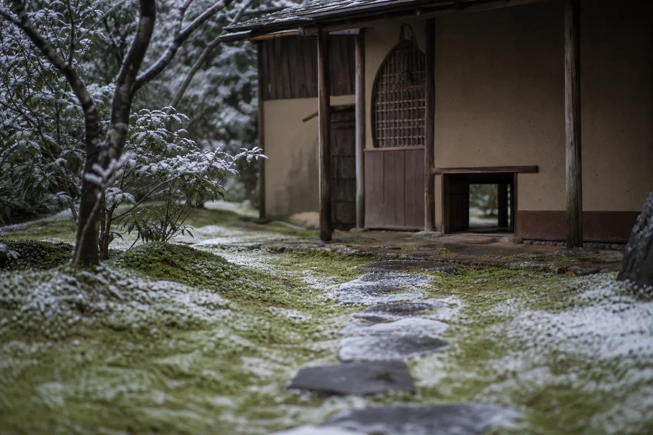 A sukiya-style teahouse with a low crawl-through nijiriguchi entrance at the end of a moss-lined stone path