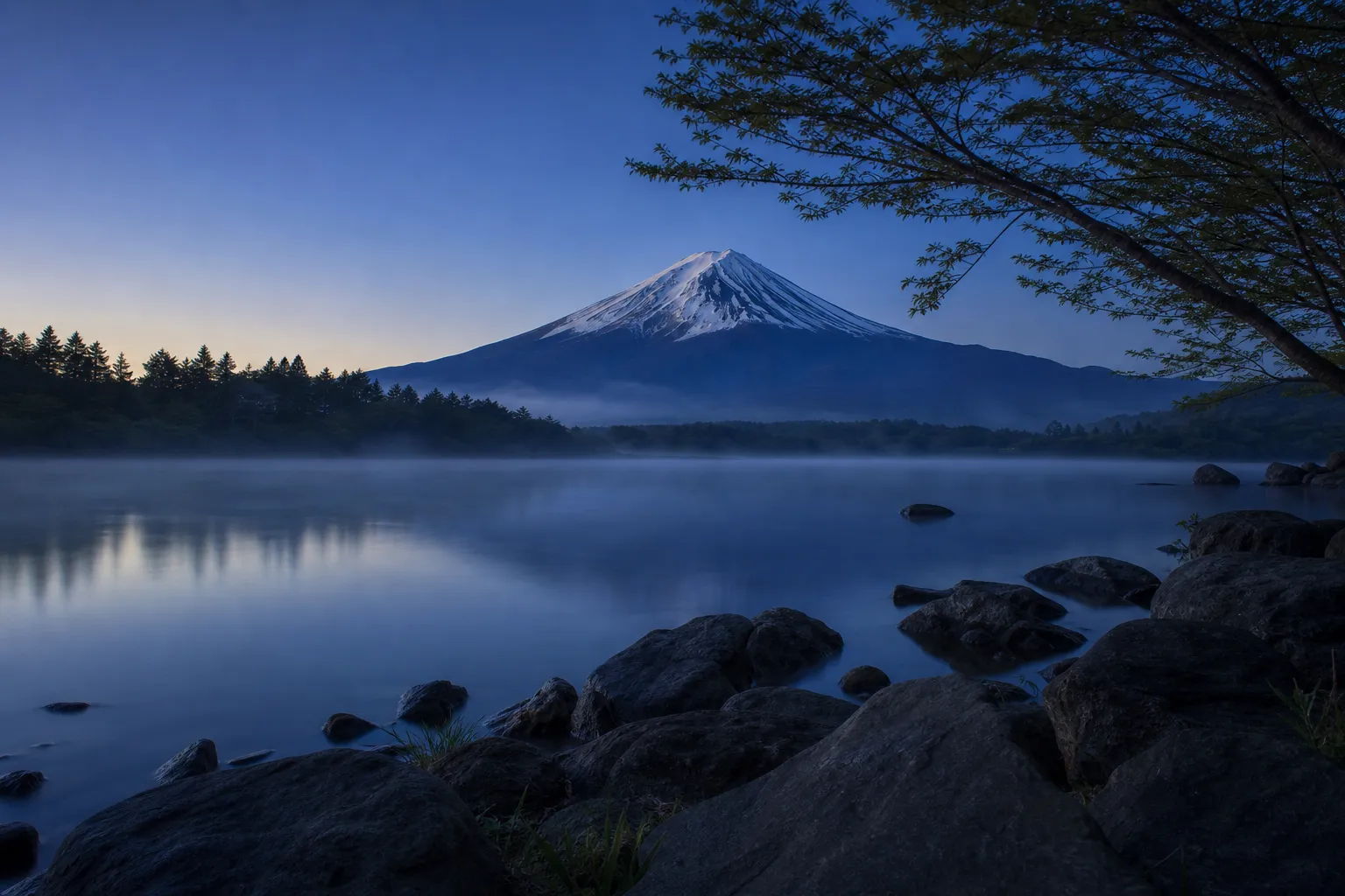Mount Fuji at sunrise reflected in a calm lake with mist over the forests, snow on the summit