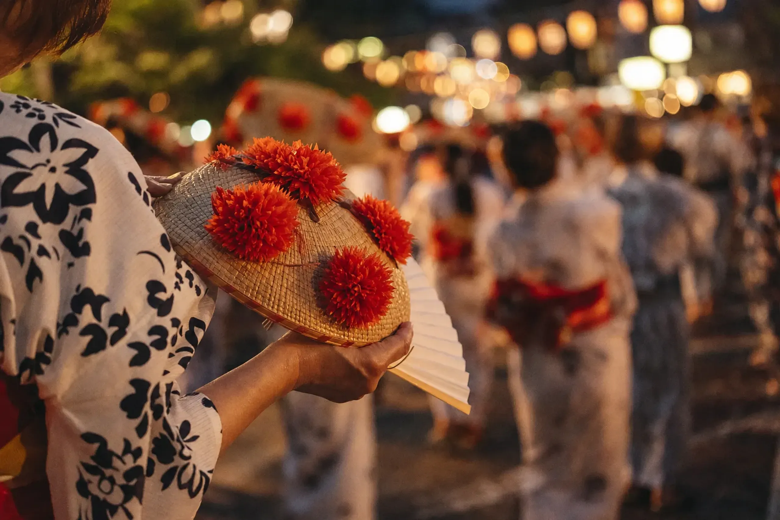 A free paper fan and a straw hanagasa hat trimmed with red benibana safflowers held by a visitor stepping into the opening dance circle near the finish