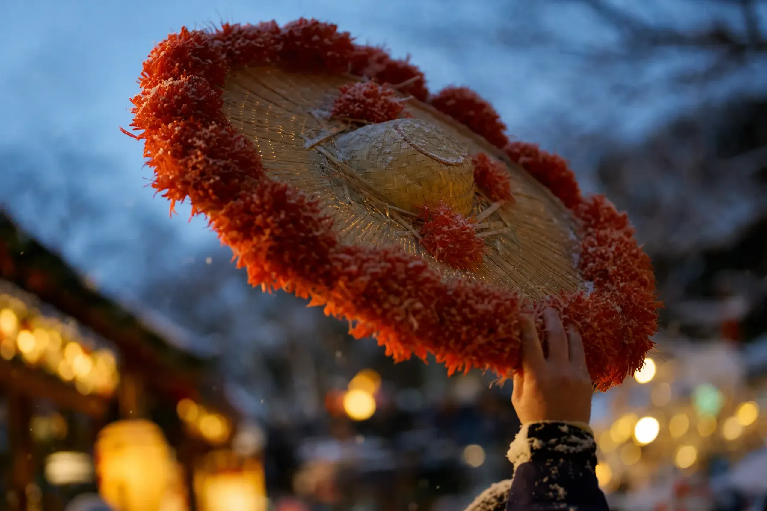 Close-up of a Yamagata Hanagasa straw hat edged with bright red safflower blossoms raised mid-turn against the evening parade route
