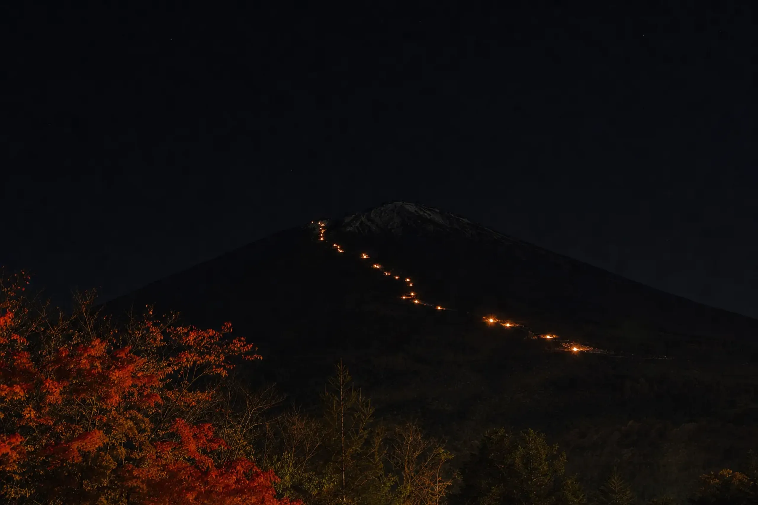 mountain-hut torches lit along the Yoshida climbing trail on Mount Fuji's slope, fire appearing to climb the mountain on a clear night