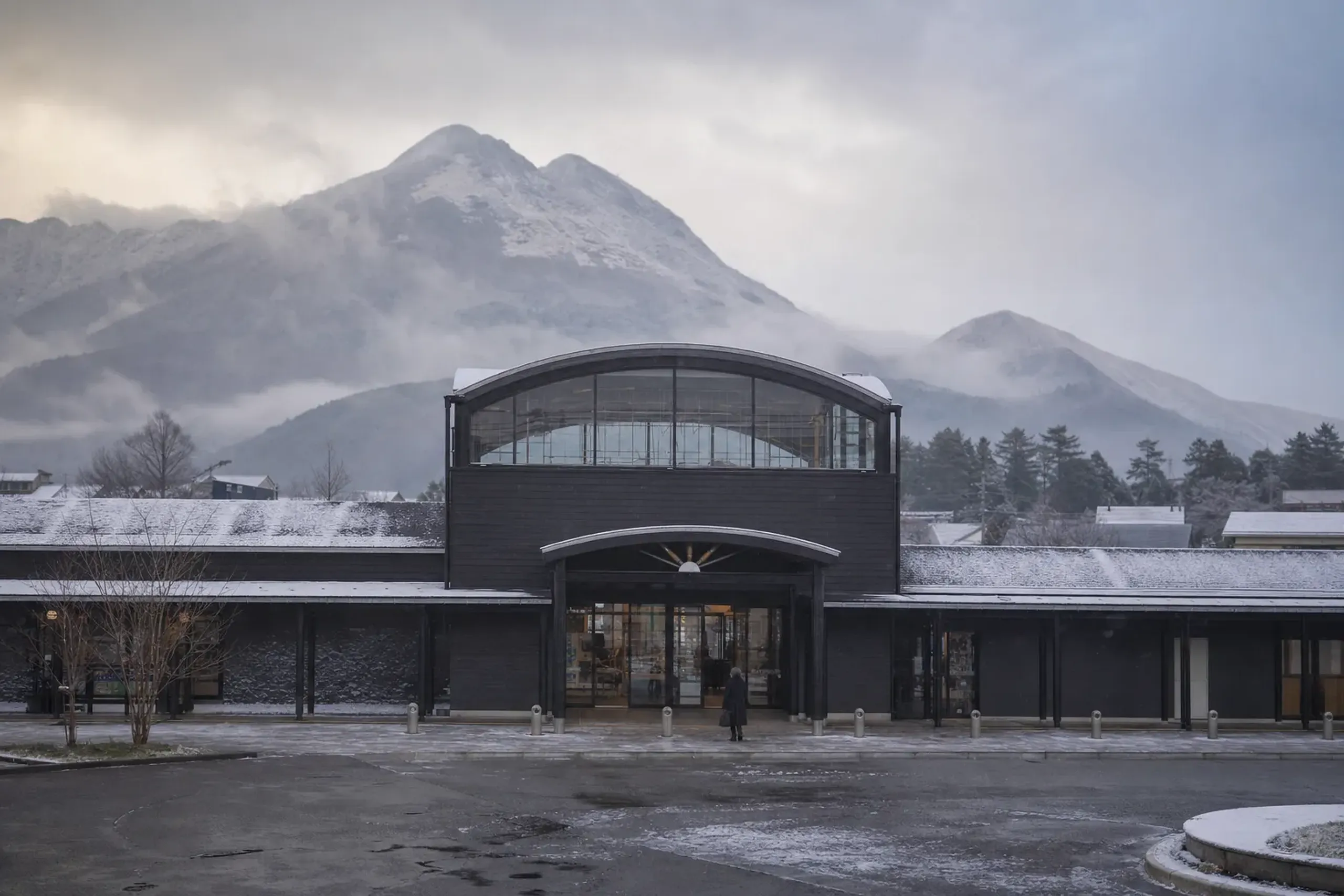 The exterior of Yufuin Station and the entrance to the Yufu City tourist information area, with the mountain basin skyline behind
