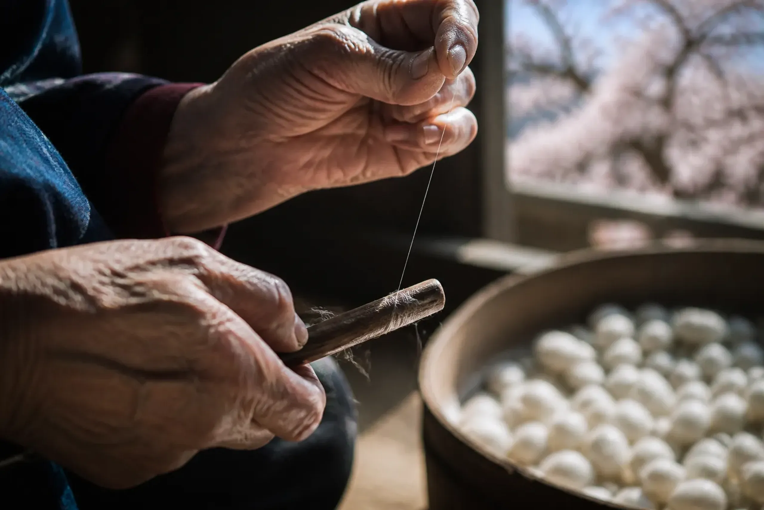 Hands drawing untwisted silk thread for Yuki tsumugi using traditional tools