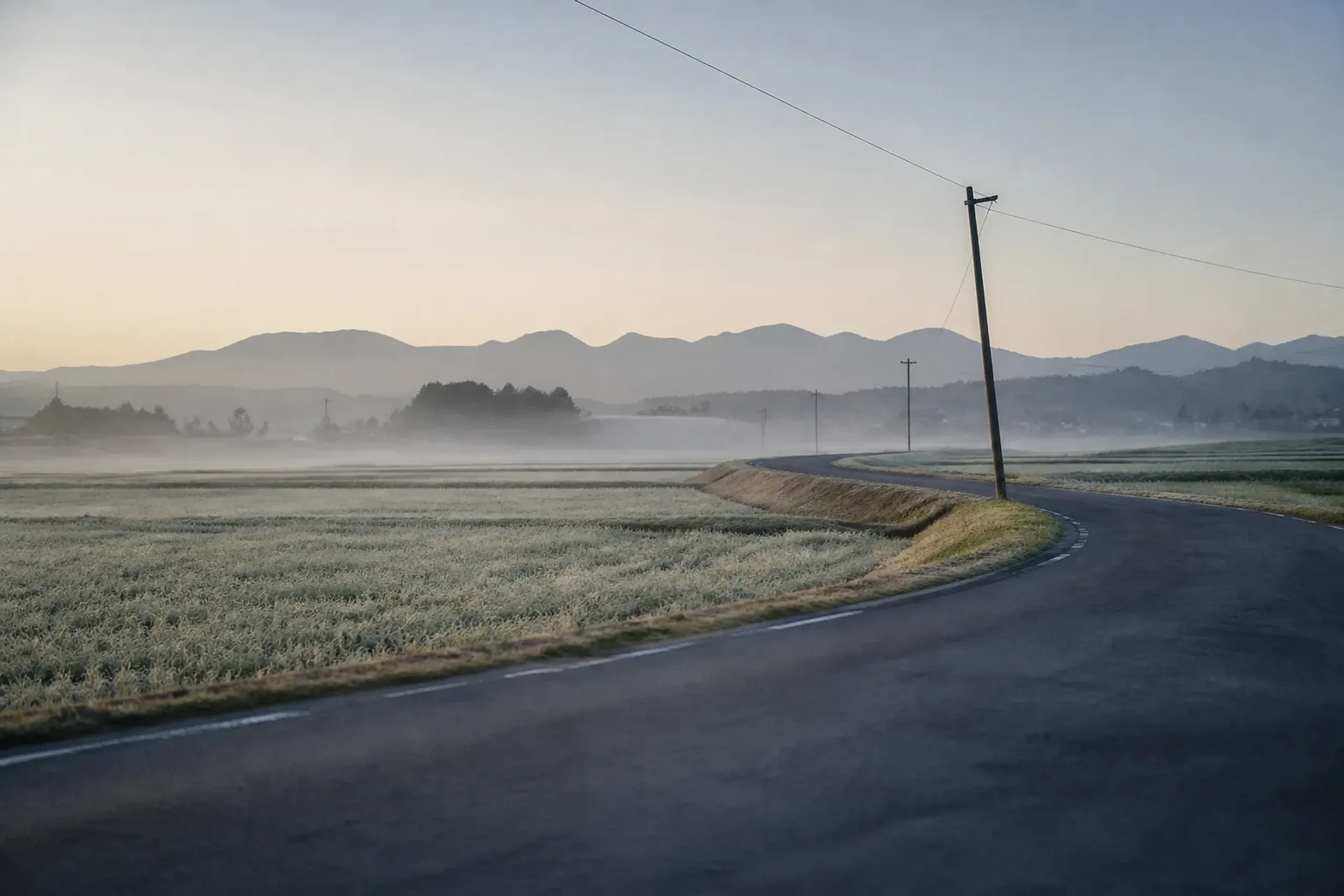 a quiet country road winding between Yūki in Ibaraki and Oyama in Tochigi, framed by rural fields and low hills