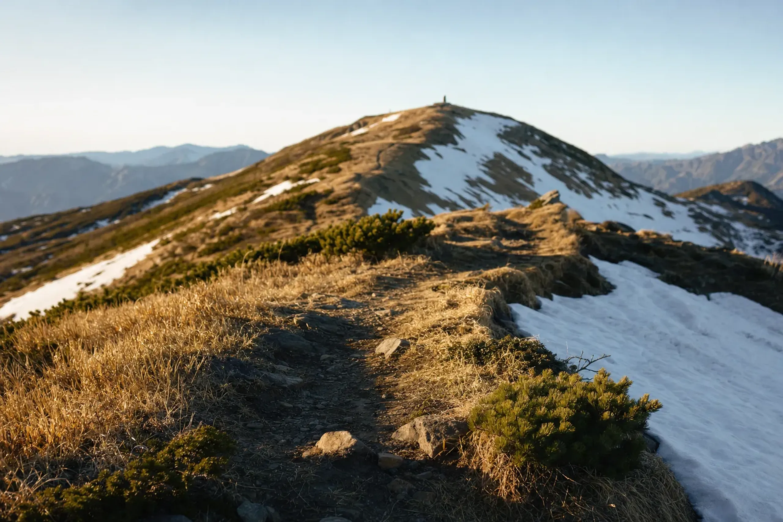 Ridgeline trail toward Kumano-dake at 1,841 metres with lingering snow in hollows and drying ridges under spring sun