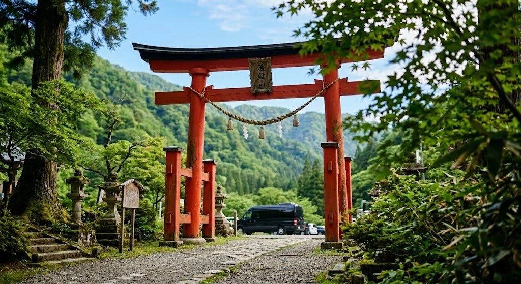 Red torii gate at shrine entrance along a gravel path, with stone lanterns and lush green trees surrounding it.