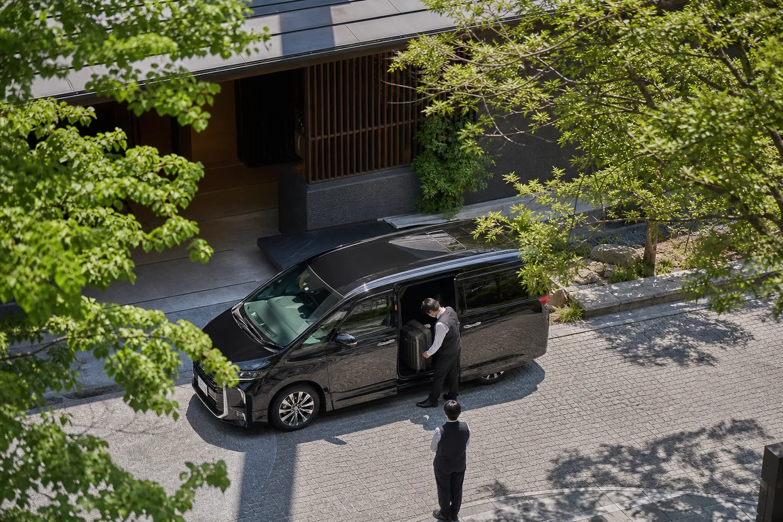 A discreet black chauffeur vehicle outside an Osaka hotel entrance with luggage being loaded